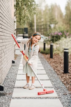 A little girl with a brush cleans a path on the street in the courtyard.