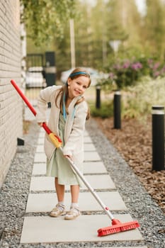 A little girl with a brush cleans a path on the street in the courtyard.