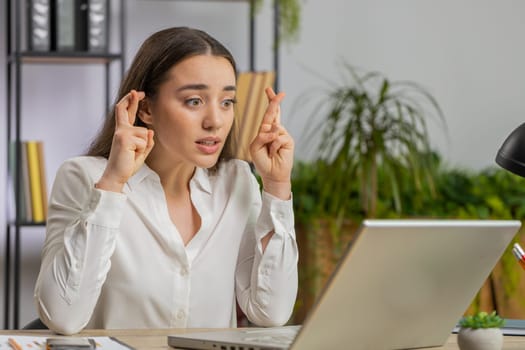 Young amazed business woman girl crossed fingers looking at laptop screen asking for good luck news, wishing good exam results, dreaming about win victory in lottery jackpot, money profit at office