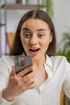 Oh my God, Wow. Happy amazed young business woman working on smartphone shocked by sudden victory, game winning, lottery goal achievemen good news. Pretty manager girl freelancer at office. Vertical