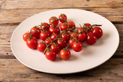 High angle view of fresh red cherry tomatoes in white plate on wooden table. unaltered, organic food and healthy eating concept.