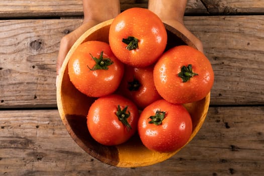 Cropped hands holding bowl of fresh tomatoes over wooden table. unaltered, organic food and healthy eating concept.