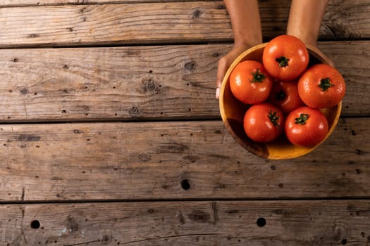 Directly above view of cropped hands holding fresh tomatoes in bowl on wooden table. unaltered, organic food and healthy eating concept.