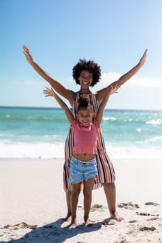 Full length portrait of happy african american mother and daughter with arms raised at beach. unaltered, family, lifestyle, togetherness, enjoyment and holiday concept.