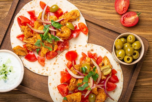 Cooking Traditional Greek Dish Gyros: Closeup of Pita bread with vegetables, meat, herbs, olives on rustic wooden cutting board with Tzatziki sauce, olive oil from above .