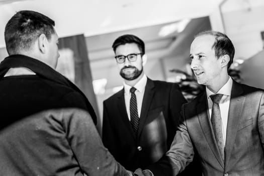Group of confident business people greeting with a handshake at business meeting in modern office. Closing the deal agreement by shaking hands. Black and white image.