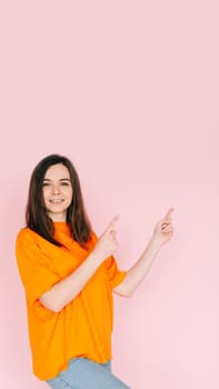 Inviting Emptiness: Cheerful Woman Pointing with Two Fingers to an Empty Space - Drawing Attention to Available Opportunities, Isolated on Pink Background.