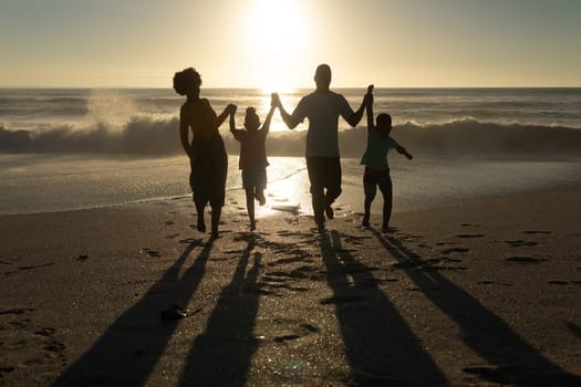 Happy african american parents enjoying sunset with children at beach against sky. unaltered, family, lifestyle, togetherness, enjoyment and holiday concept.