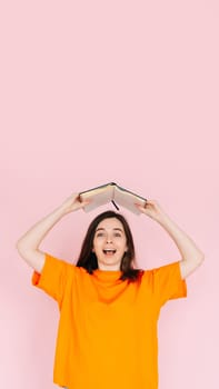 Joyful Book Enthusiasm: Cheerful Woman Holding Book Overhead with Exuberance - Delightful Mood and Positivity Concept, Isolated on Pink Background