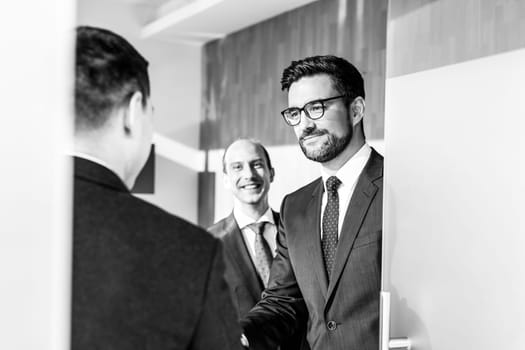 Group of confident business people greeting with a handshake at business meeting in modern office. Closing the deal agreement by shaking hands. Black and white image.