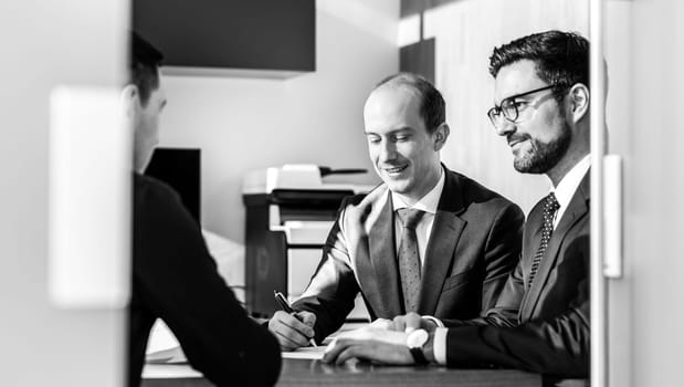 Team of confident successful business people reviewing and signing a contract to seal the deal at business meeting in modern corporate office. Business concept. Black and white image.