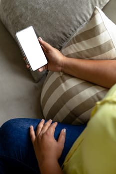 High angle midsection of african american mid adult woman using smart phone on sofa at home. unaltered, copy space, wireless technology, lifestyle and domestic life concept.