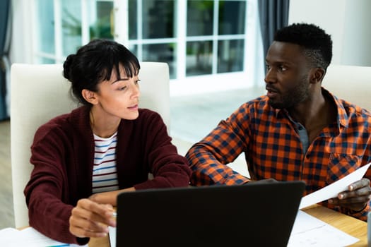 Multiracial young couple discussing household expense budget over laptop and bills at home. unaltered, lifestyle, togetherness, finance, planning, calculating, savings.