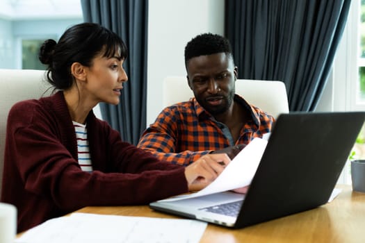 Multiracial young couple discussing household expense budget over bills and laptop at home. unaltered, lifestyle, togetherness, finance, planning, calculating, savings.