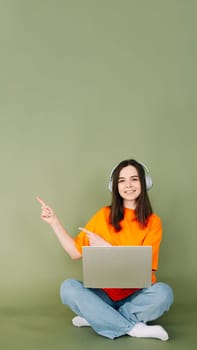 Professional young woman working with a modern laptop gadget and confidently pointing with two fingers to an empty space, perfectly designed for text and advertising Isolated green colored background