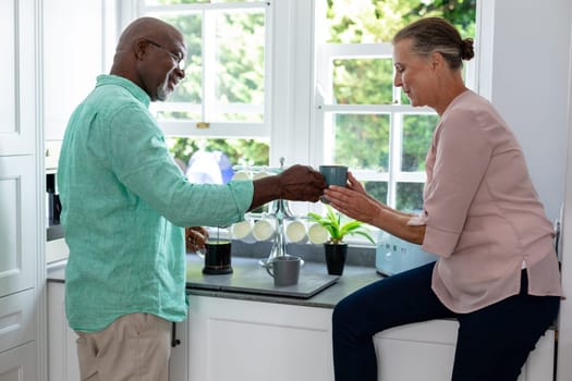 Senior multiracial couple having coffee in kitchen at home. unaltered, lifestyle, retirement, togetherness, drink, refreshment.