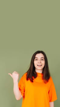 Cheerful lady in stylish orange clothing points to empty advertising space. Perfect for affordable promotions. Isolated on green background