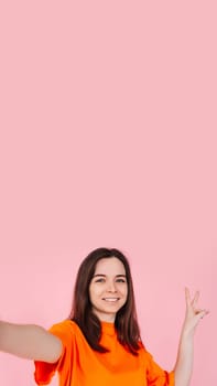 A vivaciously stunning girl with a radiant smile, confidently showing the V sign with her fingers. On a pink background. Blank space to add text or graphics for party, holiday and promotional design.