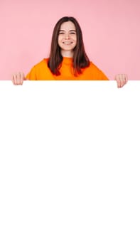 Surprised Woman Holding White Promo Paper for Unexpected Best Deal Offer. Expressive Shock and Excitement. Isolated on Pink Background. Perfect for Advertising, Marketing, and Promotional Concepts.