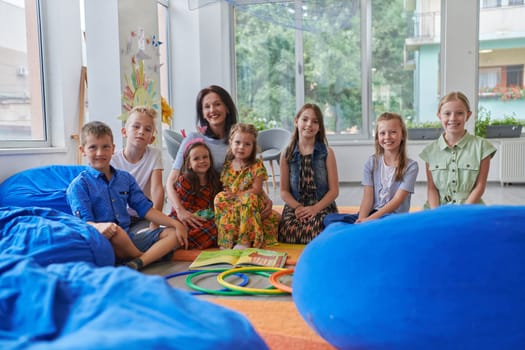 A happy female teacher sitting and playing hand games with a group of little schoolchildren.