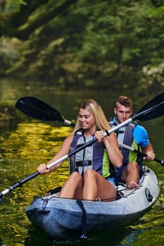 A young couple enjoying an idyllic kayak ride in the middle of a beautiful river surrounded by forest greenery.