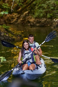 A young couple enjoying an idyllic kayak ride in the middle of a beautiful river surrounded by forest greenery.