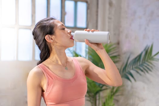 Beautiful sporty asian woman drinking water from a canteen. Healthy lifestyle concept. High quality photo