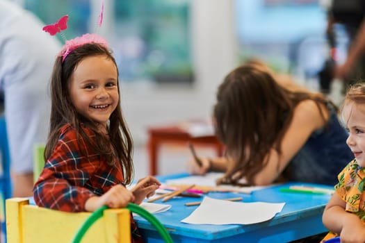 Creative kids during an art class in a daycare center or elementary school classroom drawing with female teacher