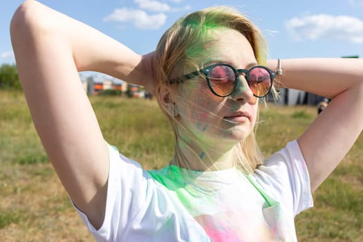 Closeup Beautiful Caucasian Blond Woman With Colorful Dye, Powder On Face, Cloth On Holi Colors Festival In Park, Sunny Day. Playful Cultural Event With Throwing Bright Neon Powder. Horizontal Plane.
