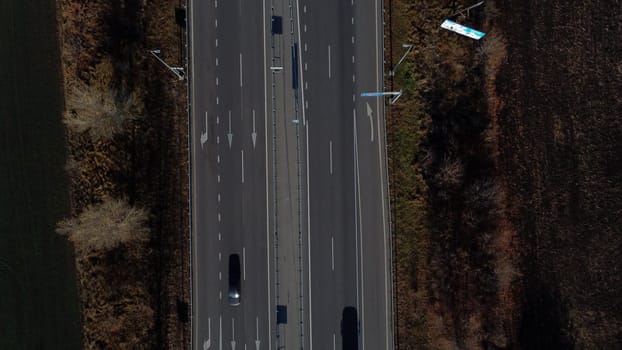 Cars driving along highway on autumn sunny day. View of cars driving on paved road. Top view. Automobile road with white markings between agricultural fields. Aerial drone view.Automobile vehicles.