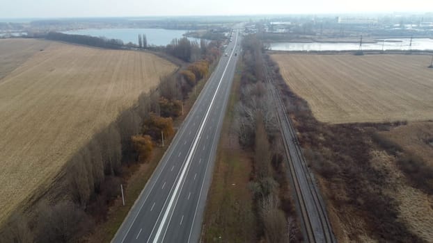 Landscape Highway, driving cars, agricultural fields after harvest, lakes on autumn day. Flying over automobile asphalt road with white markings and many cars. Perspective scenery. Aerial drone view