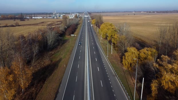 Cars driving along the highway on an autumn sunny day. Automobile road with white markings between agricultural fields. View of the cars driving on paved road. automobile vehicles. Aerial drone view..