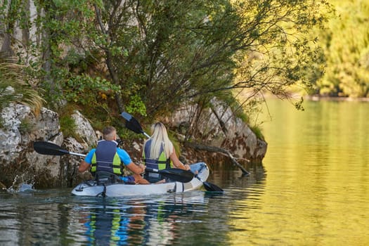 A young couple enjoying an idyllic kayak ride in the middle of a beautiful river surrounded by forest greenery.