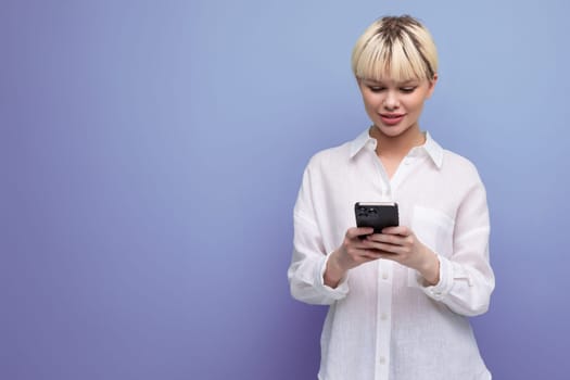 young pretty caucasian office worker woman with short blond hair dressed in a white blouse uses a smartphone on the background with copy space. business concept.