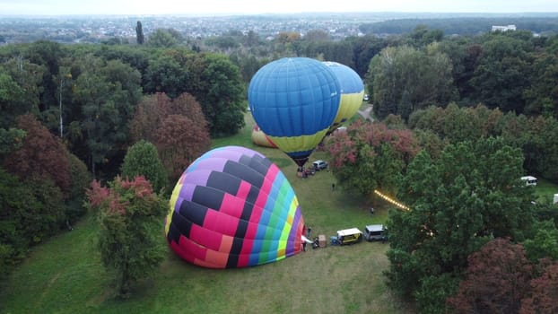 Balloon Festival. Inflating big balloon aerostat. Several air balloons lie on ground and inflate in meadow in forest. Balloon aerostat inflation. Fire flame. Entertainment rest, recreation, travelling