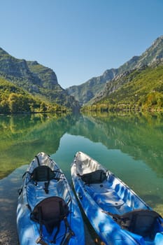 An idyllic photo of two kayaks on the river bank. In the background of green forest area and mountains.
