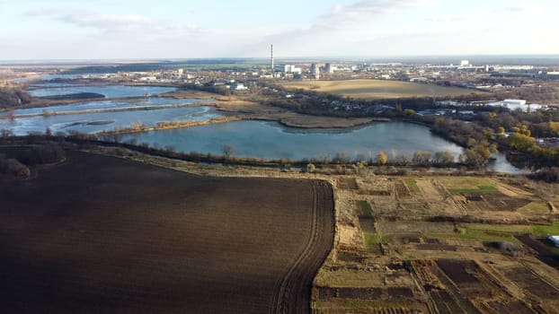 Urban beautiful landscape agricultural plowed fields, lakes for growing fish, gardens, plants,building industrial area of city, cloud shadows on sunny autumn day. Aerial drone view.