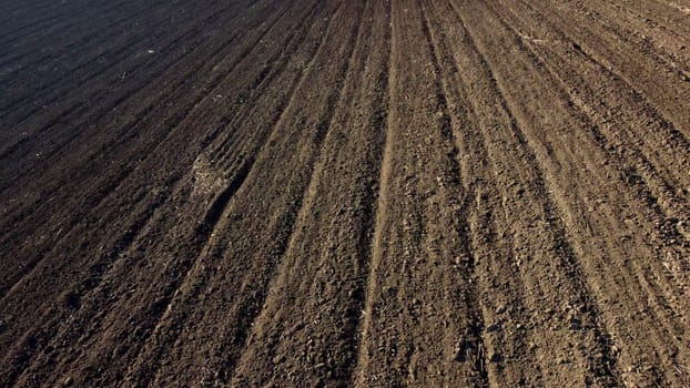 Landscape of plowed up land on an agricultural field on a sunny autumn day. Ground earth dirt priming aerial drone view. Black soil. Agrarian background. Flying over the plowed earth with black soil.