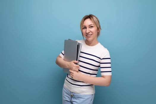 portrait photo of a confident business woman in a casual striped sweater with a laptop computer in her hands on a blue background.