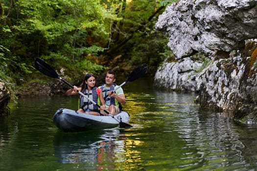 A young couple enjoying an idyllic kayak ride in the middle of a beautiful river surrounded by forest greenery.