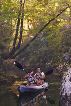 A young couple enjoying an idyllic kayak ride in the middle of a beautiful river surrounded by forest greenery.