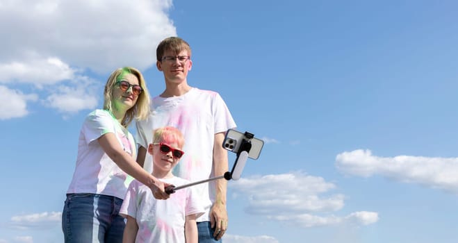 Caucasian Family Takes Selfie. Parent And Child With Colorful Dye At Birthday Party Or Celebrating Holi Color Festival, Blue Sky On background. Cheerful Family Spend Time Together. Horizontal Plane.