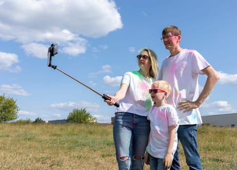 Caucasian Family Takes Selfie. Parent, Child With Colorful Dye At Birthday Party Or Celebrating Holi Color Festival, Blue Sky On background. Cheerful Family Spend Time Together. Horizontal Copy Space