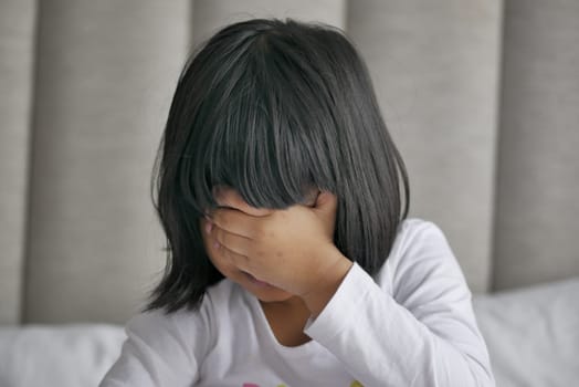 a upset child girl cover her face with hand .