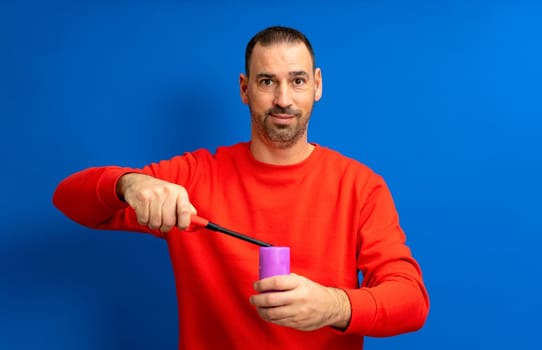 Hispanic man with a beard lighting a purple candle with a kitchen lighter, isolated on a blue studio background