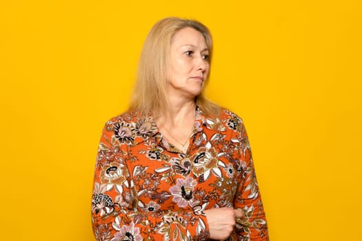 Portrait of a blonde Caucasian woman in her 40s with a serious melancholy face looking to the side with pity, isolated over yellow studio background