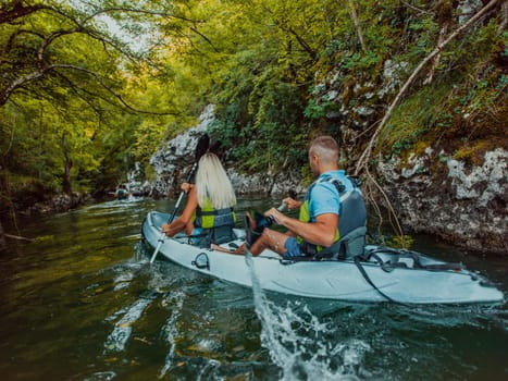 A young couple enjoying an idyllic kayak ride in the middle of a beautiful river surrounded by forest greenery.