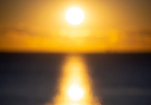 Blurred background. Sun shining in sky with clouds during sunset dawn. Sunrise dawning sundown. Sunny path, sunny walkway on surface of sea waves. Sunlight. Sea landscape. Natural blurry bokeh texture