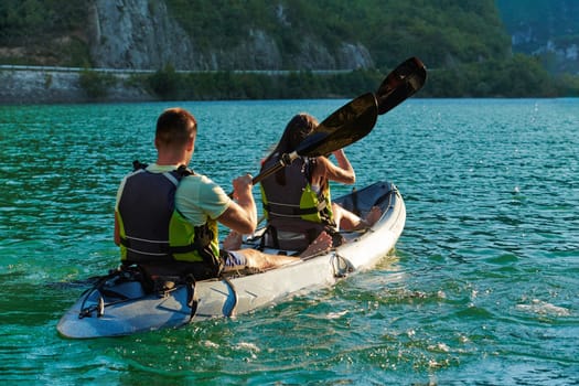 A young couple enjoying an idyllic kayak ride in the middle of a beautiful river surrounded by forest greenery in sunset time.