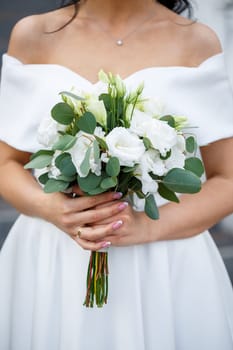 Hands of the bride close-up with a bouquet of fresh beautiful flowers. Attribute of the bride
